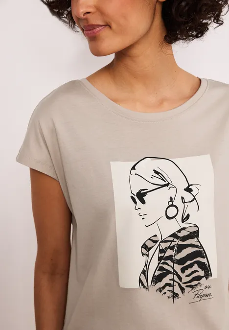 Frau trägt beiges T-Shirt mit stilisierter schwarz-weißer Porträtgrafik einer Frau mit Sonnenbrille.